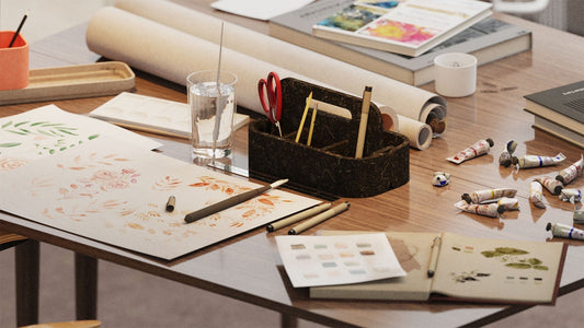Eine Aufbewahrungsbox auf einem Tisch gefüllt mit Papier, Stiften, Farben und weiteren Zeichenutensilien. Die Box besteht aus dunkelbraunem Naturfaservlies.